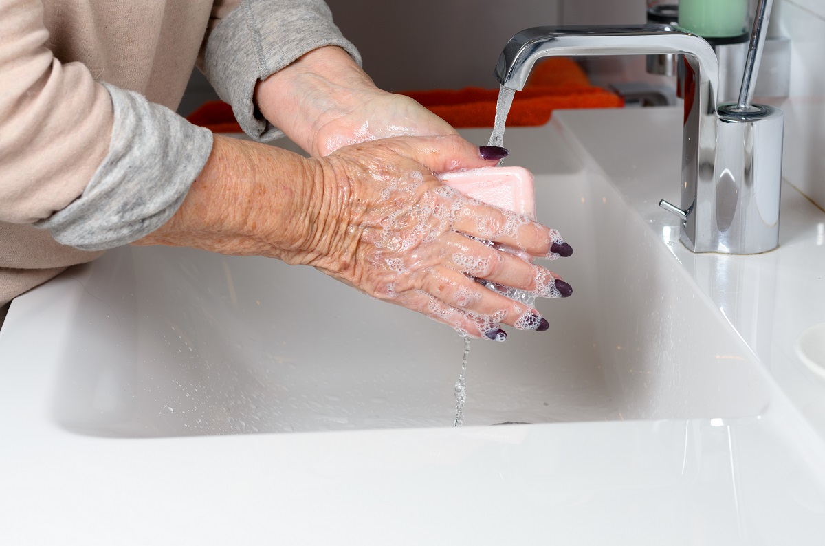 Elderly woman washing hands under tap