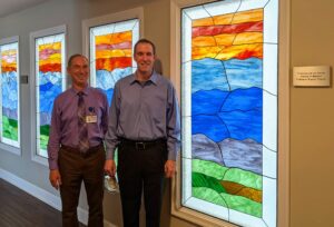 Board Chair Dan Carlton and Chaplain Hans Murdock pose next to stained glass window.