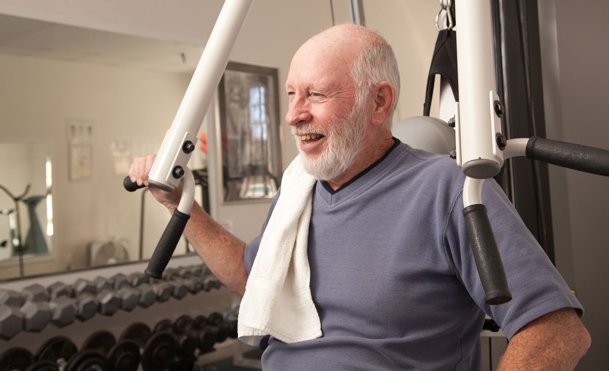 A senior man is working out on a machine in the fitness center